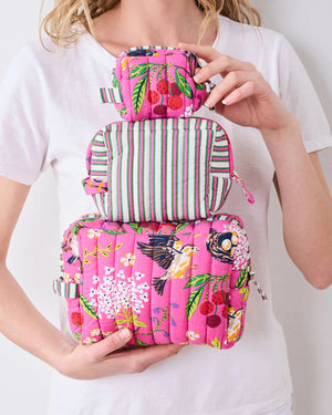 A person in a white shirt holds the PRINTFRESH - BIRD & BLOSSOM THREE POUCH SET by PRINTFRESH, featuring three quilted makeup pouches with colorful floral and striped patterns, nested from smallest to largest.