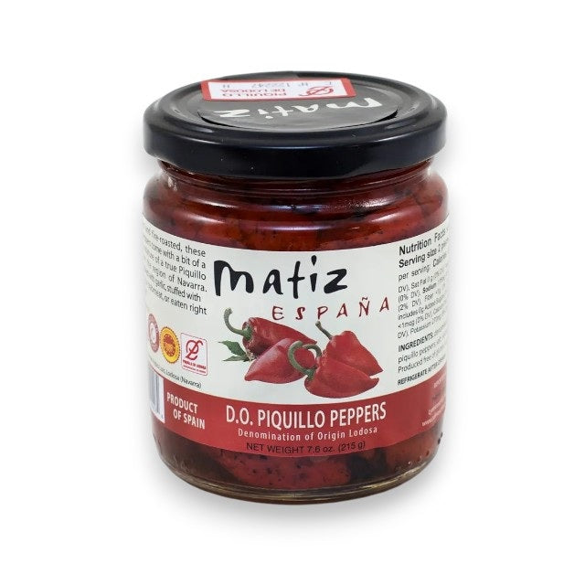 A 7.6 oz (215 g) jar of MATIZ - PIQUILLO PEPPERS by MATIZ ESPANA from Spain, featuring a clear label with illustrated peppers, product info, nutrition facts, and a black lid. These are roasted piquillo peppers.