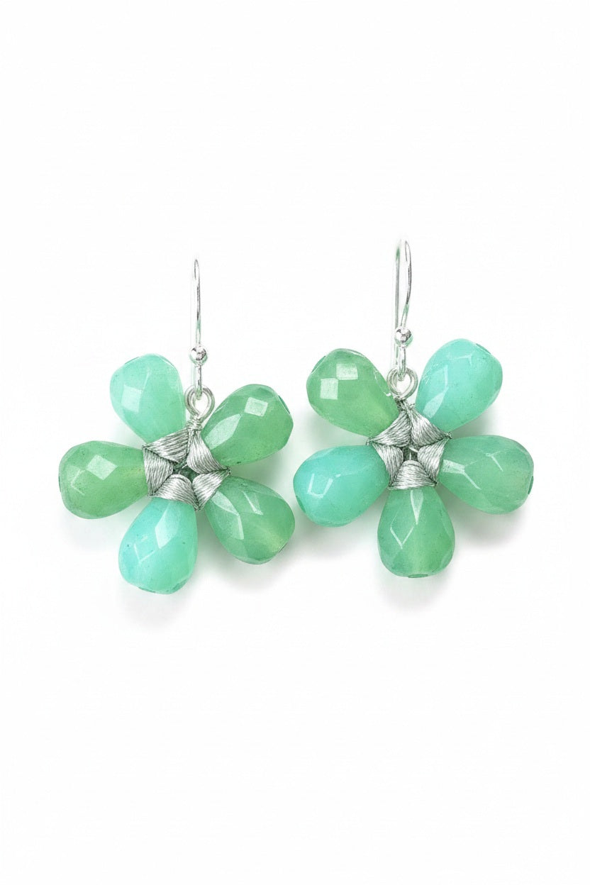 The ANN LIGHTFOOT - FACETED CHRYSOPRASE FLOWER EARRINGS by ANN LIGHTFOOT feature blossom-shaped designs crafted from five faceted green chrysoprase stones with delicate silver wire wrapping at the center, elegantly hanging from sterling silver hooks against a softly blurred, neutral background.