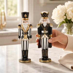 A hand places a BLACK AND WHITE NUTCRACKER with hand-painted embellishments next to an identical one on a marble countertop.