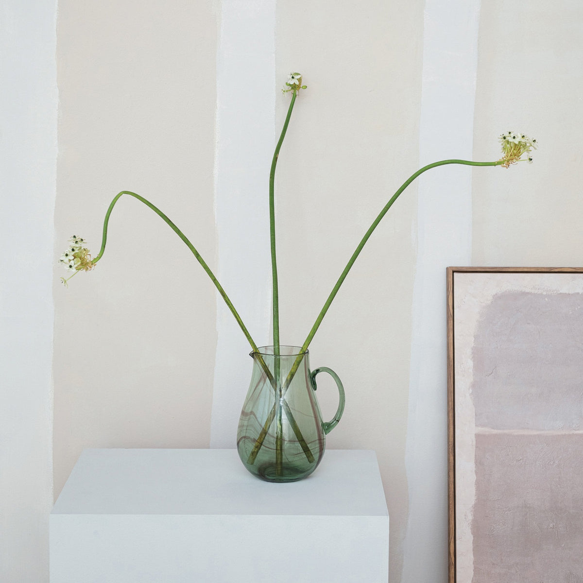 The CREATIVE COOP MARBLED GREEN AND PURPLE HAND-BLOWN RECYCLED GLASS PITCHER, featuring a curved handle and unique swirled patterns, is showcased against a plain white background.