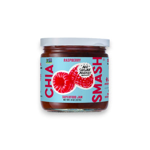 A jar of CHIA SMASH - RASPBERRY CHIA JAM. This 8 oz (227g) jar features a light blue label adorned with images of raspberries and a "NO SUGAR ADDED" text bubble. The label proudly highlights that the product is Non-GMO Project Verified, made with upcycled fruit, and suitable for both paleo and vegan diets.