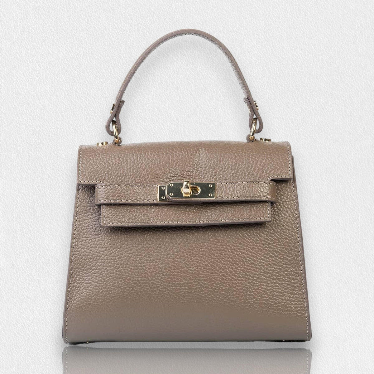 The LE BORSETTE LEATHER SATCHEL BAG is a small, structured satchel-shaped handbag in light pink, featuring a gold clasp at the front. It boasts a single top handle, an adjustable shoulder strap, and two gold-tone hardware pieces on either side of the handle. The textured leather adds to its luxurious and elegant appearance against the plain white background.