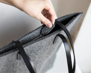 A person in a beige trench coat holds the WOOLBERRY WOOL FELT LONG TOTE BAG with black handles, standing against a plain, light-colored background.