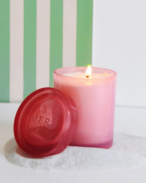 The MERSEA Cabana Flower Jolie Jar Candle features a pink cylindrical design in a translucent container with a matching lid, infused with soothing Ylang Ylang, and shown against a white background.