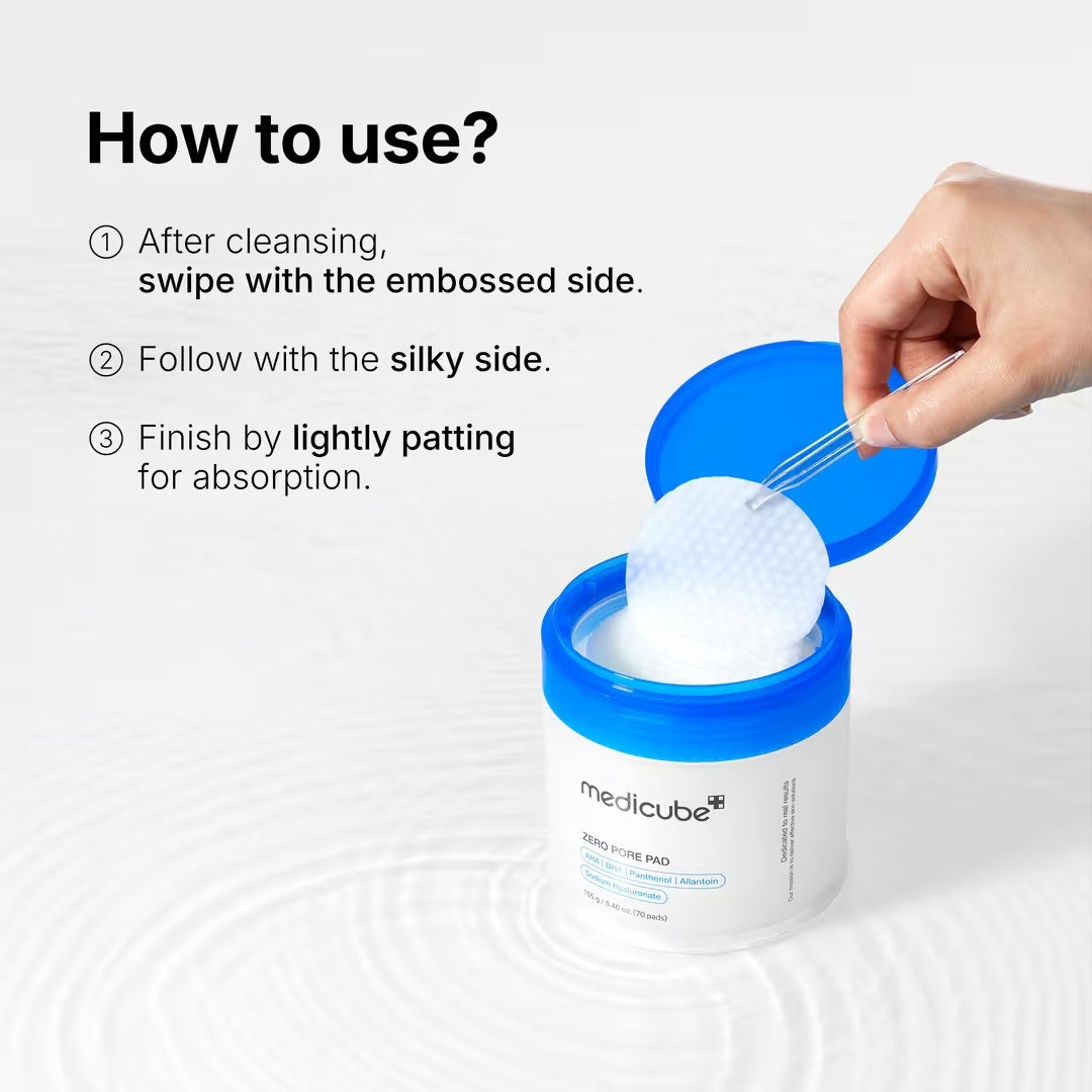 A hand holds a round, textured exfoliating pad above an open jar of KOSMIC KBEAUTY SKINCARE MEDICUBE - ZERO PORE PAD 2.0, 100ML, with its blue lid set aside on a plain white background.