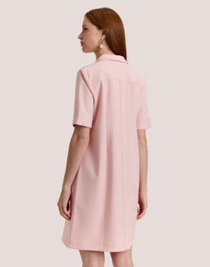 A woman with long, straight auburn hair wears the HINSON WU Bridget Short Sleeve Traveler's Twill Dress in blush pink, featuring a collar and gold front zipper, standing against a plain light background.