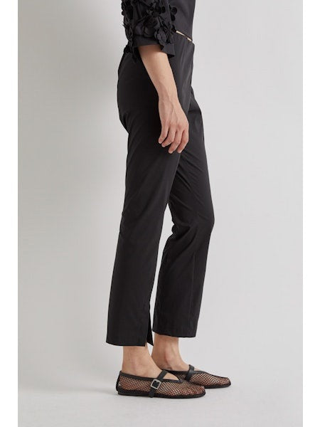 A person stands against a plain background wearing MEIMEIJ FROTN HEM SPLIT COTTON PANT—black, cropped, ankle-length pants with small slits. They also wear a black textured-sleeve top and black shoes. Their face is not visible in the image.