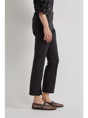 A person stands against a plain background wearing MEIMEIJ FROTN HEM SPLIT COTTON PANT—black, cropped, ankle-length pants with small slits. They also wear a black textured-sleeve top and black shoes. Their face is not visible in the image.