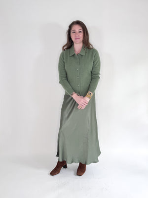 The ROSE & CROWN - CASHMERE CARDIGAN, a luxury long-sleeve button-up in custom-dyed magenta, hangs on a white hanger against a light gray background.