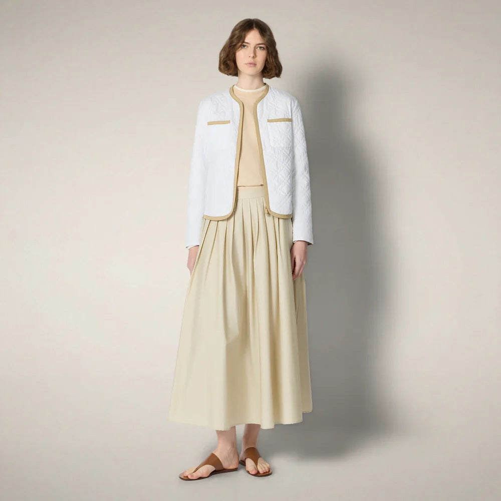 A woman with short brown hair wears the SAVE THE DUCK - JALINA Puffer Jacket by SAVE THE DUCK, featuring diamond quilting and tan trim, paired with a cream skirt, against a plain, light background.