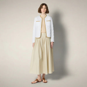 A woman with short brown hair wears the SAVE THE DUCK - JALINA Puffer Jacket by SAVE THE DUCK, featuring diamond quilting and tan trim, paired with a cream skirt, against a plain, light background.