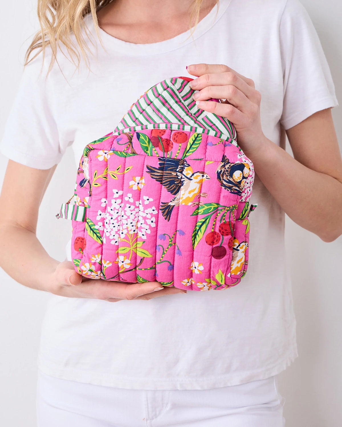 A person in a white shirt holds the PRINTFRESH - BIRD &amp; BLOSSOM THREE POUCH SET by PRINTFRESH, featuring three quilted makeup pouches with colorful floral and striped patterns, nested from smallest to largest.