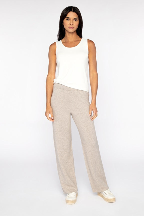 Wearing a white sleeveless top and KINROSS CASHMERE&#39;s Doublenit Cotton Cashmere pants, a person stands against a plain backdrop. Their look is complemented by white shoes, while their long dark hair adds timeless charm.