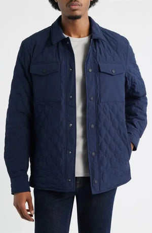 A man wears the SAVE THE DUCK Anton Jacket in navy—a dark blue, water-resistant jacket with buttoned chest pockets and a collar—paired with dark pants, standing against a plain white background.
