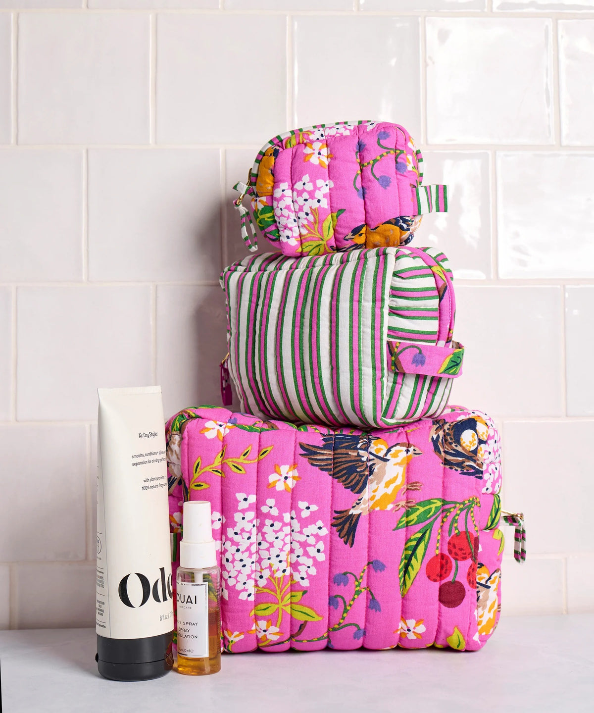A person in a white shirt holds the PRINTFRESH - BIRD &amp; BLOSSOM THREE POUCH SET by PRINTFRESH, featuring three quilted makeup pouches with colorful floral and striped patterns, nested from smallest to largest.
