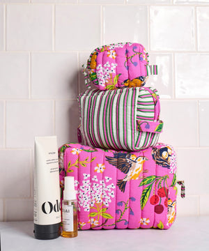A person in a white shirt holds the PRINTFRESH - BIRD & BLOSSOM THREE POUCH SET by PRINTFRESH, featuring three quilted makeup pouches with colorful floral and striped patterns, nested from smallest to largest.