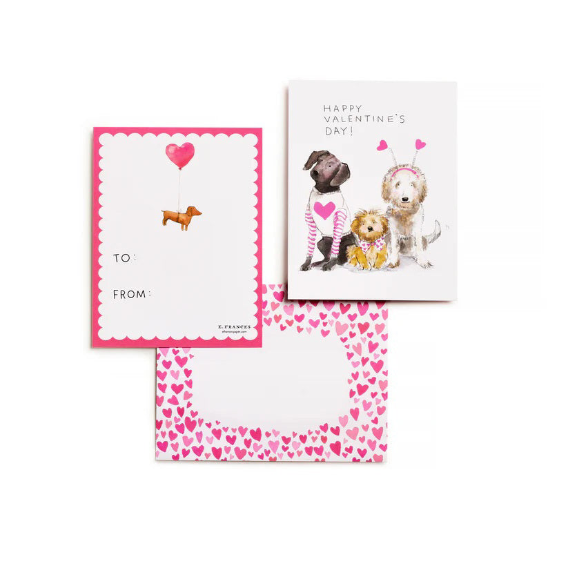 The E. FRANCES PAPER - DOGGIE DRESS-UP CLASSROOM VALENTINE SET features three dogs dressed festively: one in striped pajamas, another with a heart bandana, and a third with heart antennae. “Happy Valentine’s Day!” is displayed across the top against a backdrop of pink hearts, ideal for charming Valentines or envelopes.
