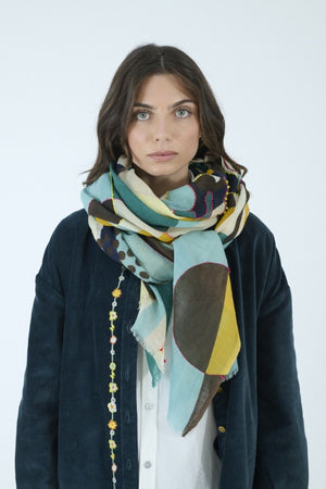 Introducing the STORIATIPIC - BAO Wool Scarf with Embroidery in Blue by STORIATIPIC: a generously sized (100 x 200 cm) wool scarf featuring a modern geometric pattern in teal, mustard yellow, brown, black, and white. Adorned with embroidered circles, dots, and rectangular motifs for a soft texture, this lightweight accessory is finished with frayed edges for added style.