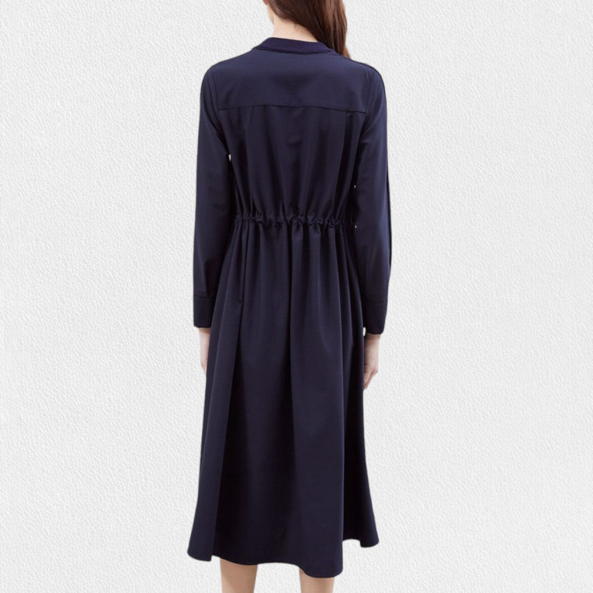 A woman models the MEIMEIJ - WOOL MIX MEDIA DRESS by MEIMEIJ, featuring long sleeves and a navy blue, knee-length wool design. She stands against a plain white textured background with her hair down and her hands relaxed at her sides.