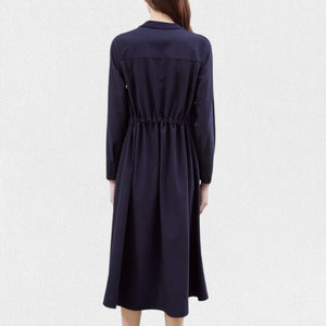 A woman models the MEIMEIJ - WOOL MIX MEDIA DRESS by MEIMEIJ, featuring long sleeves and a navy blue, knee-length wool design. She stands against a plain white textured background with her hair down and her hands relaxed at her sides.