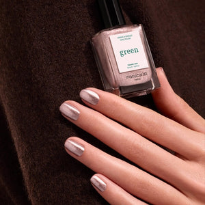 A bottle of MANUCURIST INC GREEN™ Nail Polish in the shade “Cosmic Rose,” showcasing a shimmering rose gold pink hue and topped with a black cap. The label features “green” and “quick dry intense color,” highlighting its vegan and non-toxic formula.