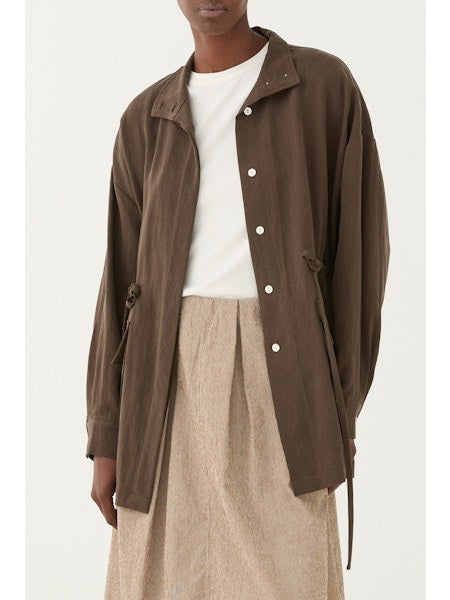 Someone wears the ELEH - JACKET WITH TIE WAIST by ELEH over a white t-shirt and a light beige textured skirt, standing against a plain light background.