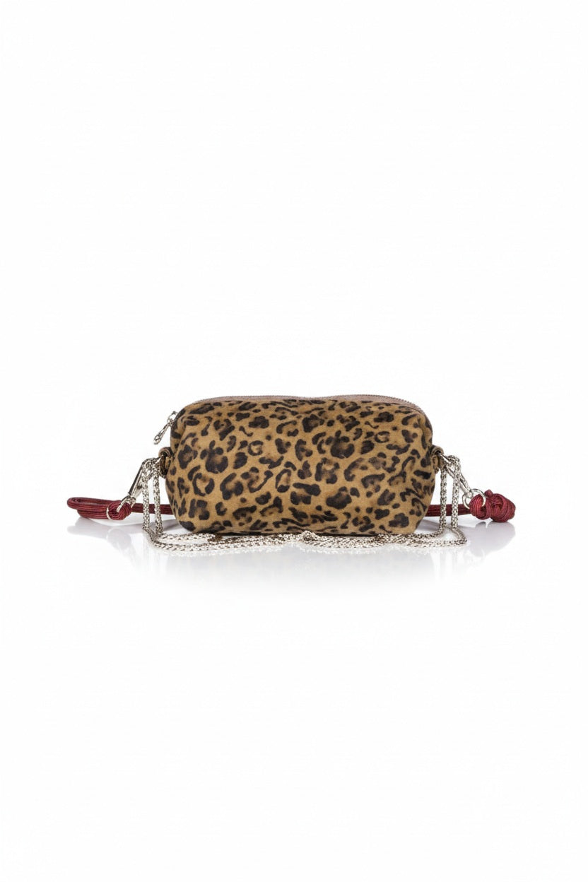 The CRAIE STUDIO - NUAGE LEO SEPIA MINI BAG, featuring a leopard print design, gold zipper, and an extended red strap, is showcased on a white pedestal against a simple backdrop.