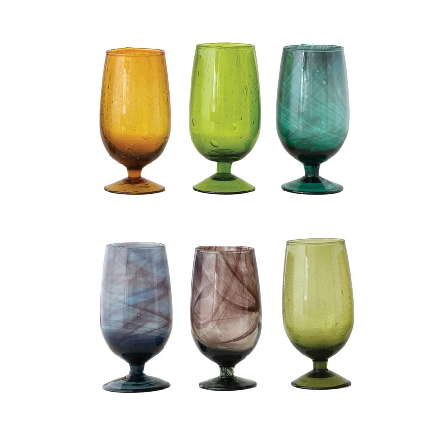 Six HAND BLOWN STEMMED DRINKING GLASS by CREATIVE COOP are arranged in two rows. Each glass features a unique swirl or bubble texture in amber, green, teal, blue, brown, or olive, showcasing artisan craftsmanship.
