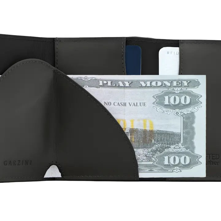 A closed black GARZINI Slim Trifold RFID-blocking leather wallet with metal card holder and coin pocket, showing the brand name on the side and cards partially visible along the edge.