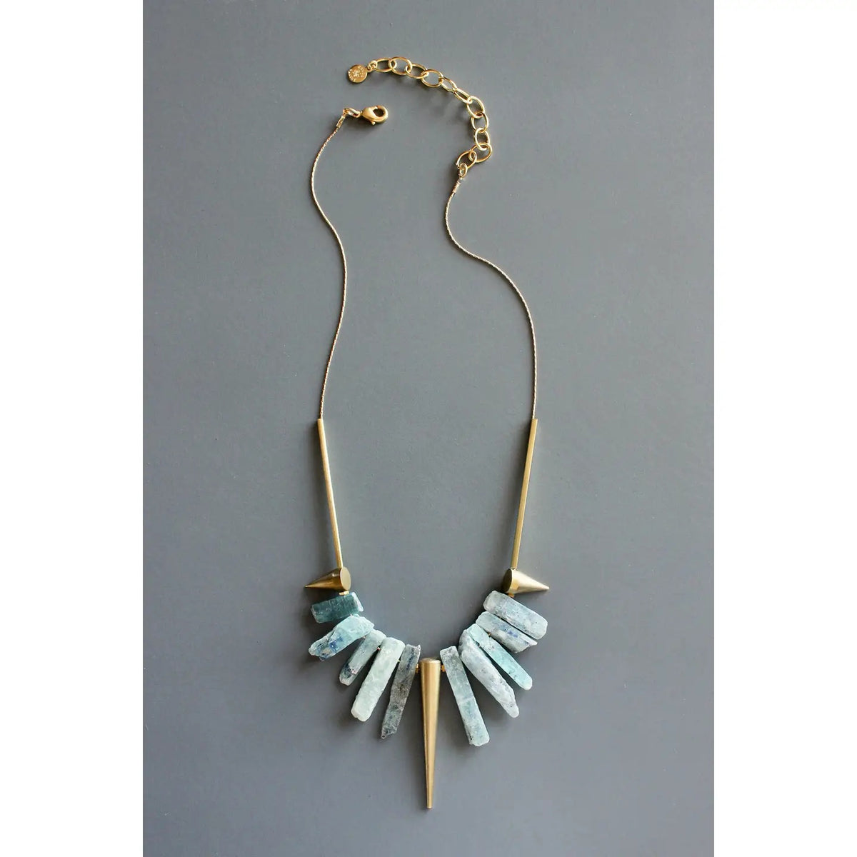 A mannequin showcases the DAVID AUBREY - KYANITE AND BRASS GEOMETRIC NECKLACE, featuring vertical blue kyanite blade beads and geometric gold bar pendants fanned out on a gold-tone plated chain against a plain background.