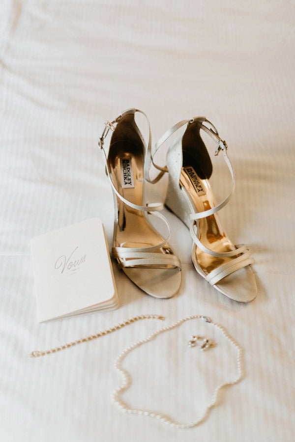 A pair of elegant, strappy high-heeled shoes, a string of pearls, a bracelet, earrings, and a booklet titled 