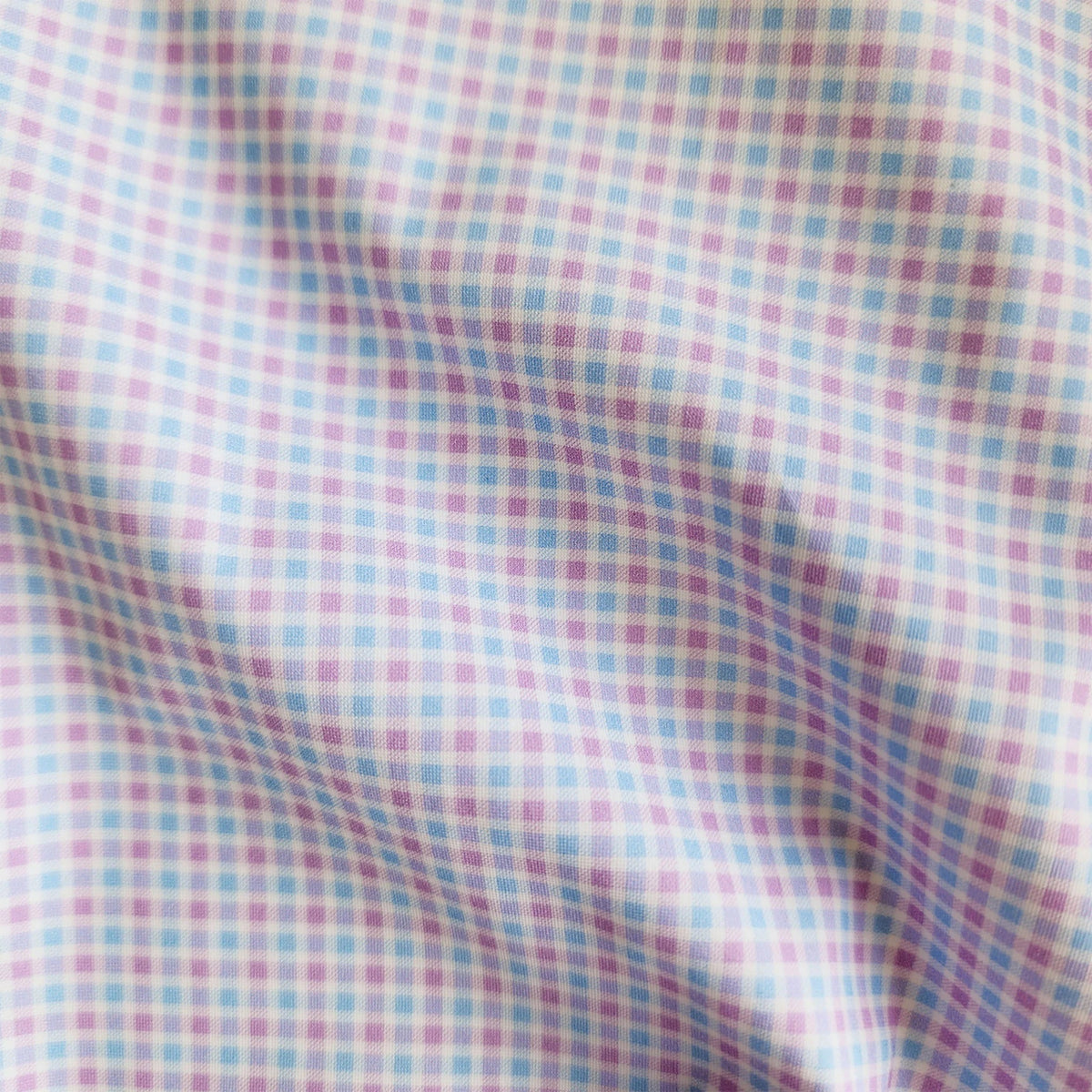A man in COLLARS AND CO's Semi Spread Collar Apex Performance Dress Shirt in Lavender and Blue Multi Gingham adjusts his collar outdoors, surrounded by green plants and a blurred background.