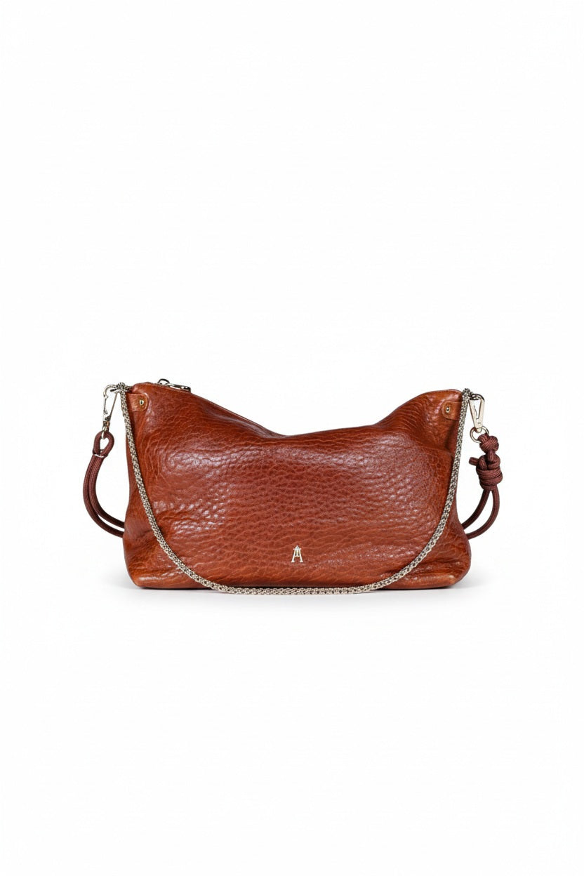 A CRAIE STUDIO - MALLOW BUBBLE CLAY HANDBAG, crafted from vegetable-tanned lambskin with a textured brown bubble leather finish, features a gold clasp and a knotted strap. The handbag is displayed on a white pedestal against a plain background.