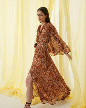 The SFIZIO - RUST PRINT RUFFLED DRESS by SFIZIO is a long, full-sleeved, flowy dress made in Italy, featuring a brown and beige spiral pattern. It boasts a V-neckline, ruffled detailing on the bodice, and an elastic waistband. Crafted from lightweight viscose creponne, it’s perfect for warm weather.