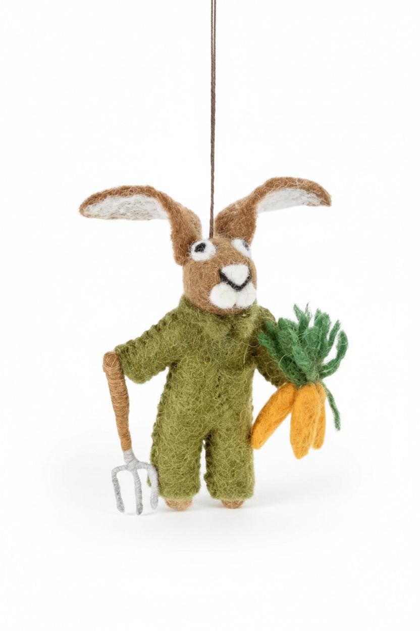 GORDON THE GARDENING HARE ORNAMENT by FELT SO GOOD, a felt hare wearing green overalls, holding a small garden fork and a bundle of carrots.