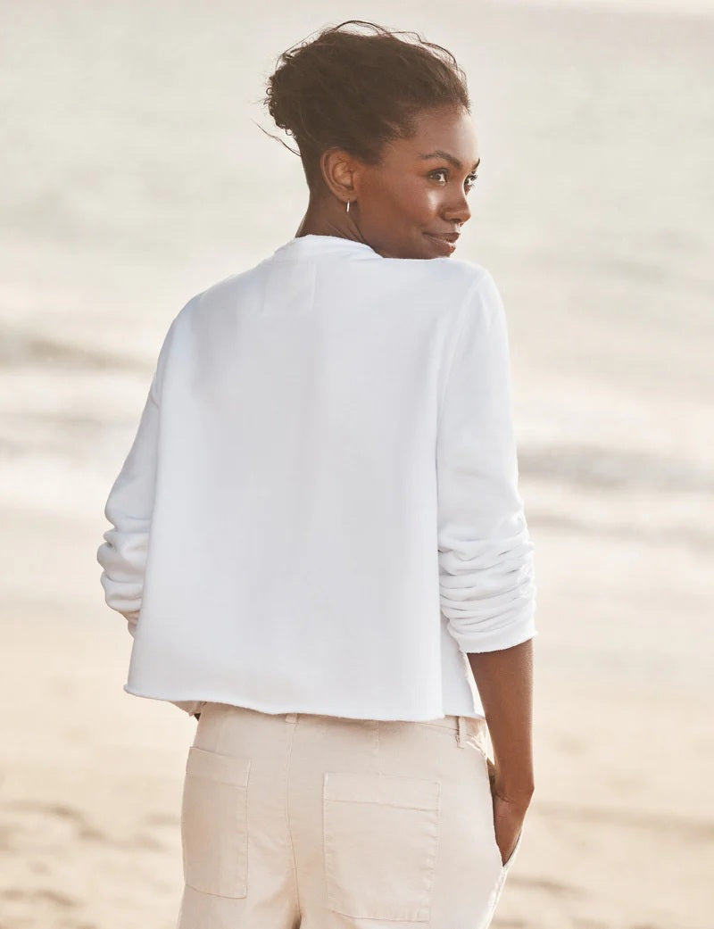 A woman stands on the beach in the FRANK &amp; EILEEN JACKIE Sweatshirt Cardigan in white, gazing sideways with the ocean and sky behind her.