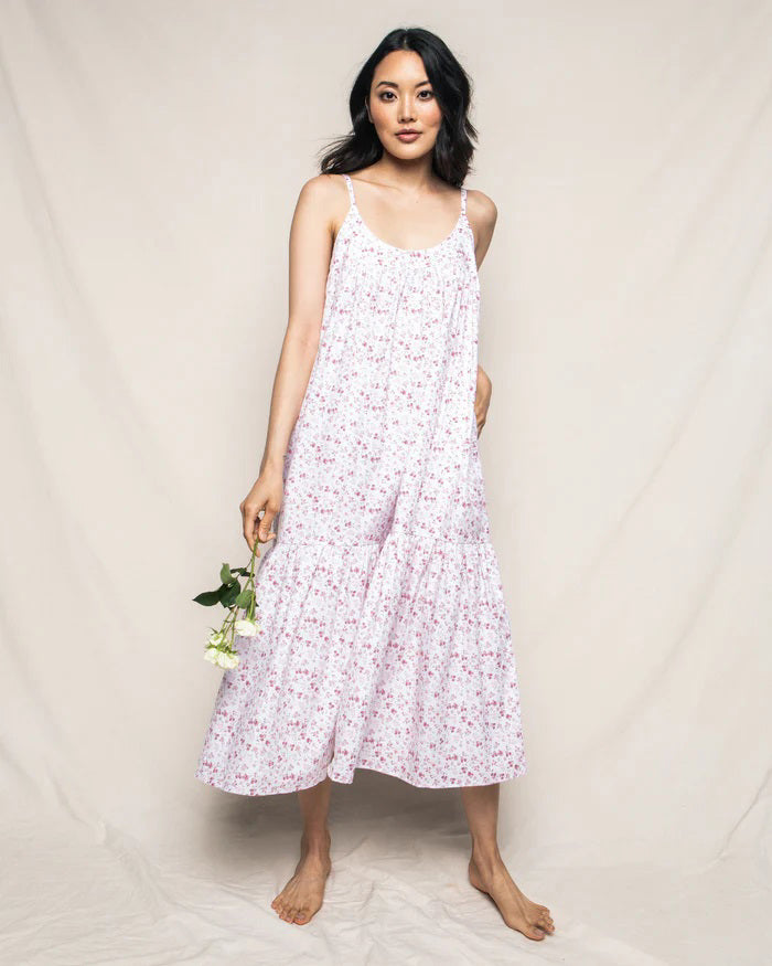 The PETITE PLUME - DORSET FLORAL CHLOE NIGHTGOWN is a sleeveless, white sundress with thin straps, reminiscent of luxurious sleepwear. It showcases a flowing, tiered design adorned with a delicate pink floral pattern. Made from the finest quality cotton, the fabric is lightweight and airy, perfect for warm weather. Displayed against a white background.
