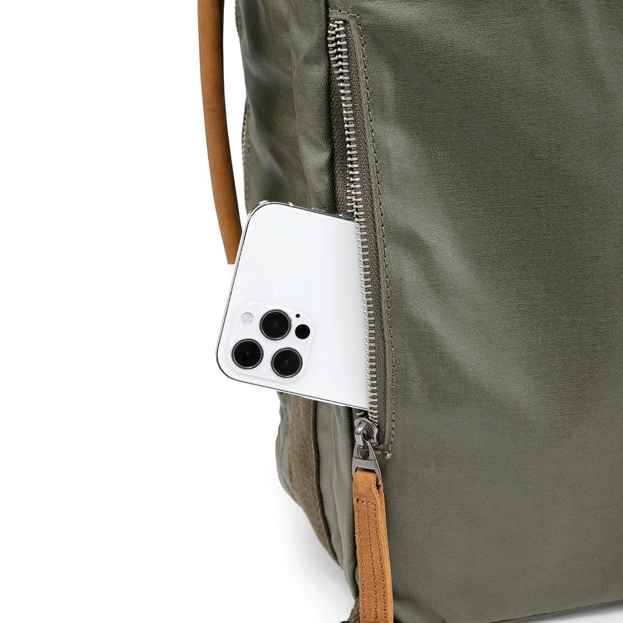 The TSD BRAND Madrone Coated Canvas Backpack in army green features brown leather accents, zippers, a top flap, side handles, metal rings, and a leather logo patch; shown lying flat to display these details.
