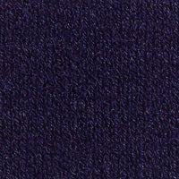 A discerning dresser with long braided hair wears the KINROSS CASHMERE EASY HI LOW VEE NECK SWEATER in orange and white pants. They stand against a plain background, smiling softly, with one hand in their pocket and the other by their side.