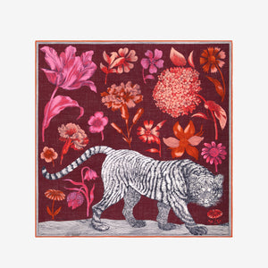 A woman with straight dark hair wears a black sweater and the INOUI EDITIONS - GUSTAV WOOL SCARF IN BURGUNDY by INOUI—a large (130 x 130 cm), multicolored patterned scarf crafted in India with cozy wool in rich red, pink, and burgundy tones—set against a plain white background.