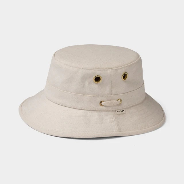 A bearded man in a white shirt wears the TILLEY - ICONIC T1 BUCKET HAT IN NATURAL with UPF 50+ protection and metal eyelets, looking directly at the camera against a plain background.