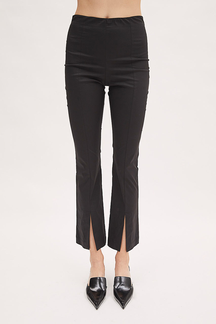 A person is modeling the MEIMEIJ Cotton Pant with Split Front Detail, which are black and high-waisted pull-on pants made of cotton. They are also wearing black pointed-toe heels. The background is plain and light-colored, focusing on the clothing.