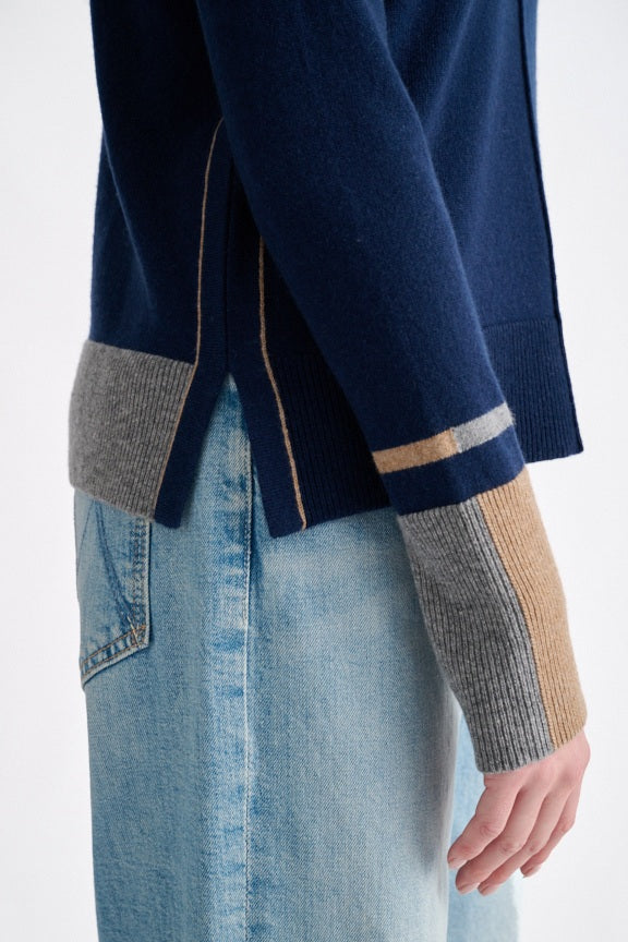 A person wearing the KINROSS CASHMERE Colorplay Crew Neck Cashmere Sweater in navy, featuring tan and gray cuffs and a classic crew neckline, pairs it with light blue jeans while standing against a plain white background and looking at the camera with a slight smile.