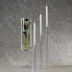 The ZODAX AMIN GLASS CANDLEHOLDER MEDIUM is a tall, clear glass holder with a sleek modern design, narrow base widening upwards, and a small top platform. Dimensions: 3.5 in x 15.75 in (8.89 cm x 40.01 cm).