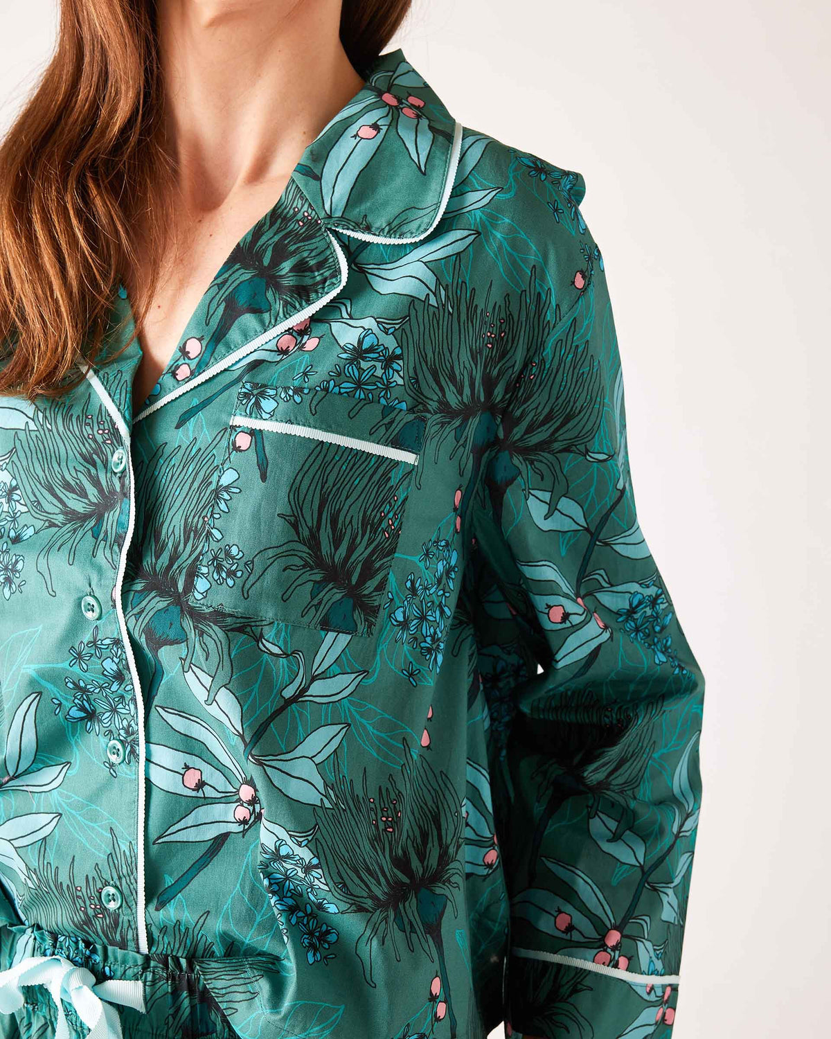 A woman stands barefoot in the MERSEA - OVER THE MOON PAJAMA SET, a 100% cotton ensemble by MERSEA with vibrant red, teal, and white vertical stripes and arrow patterns; she has her hands in her pockets and long hair over one shoulder.