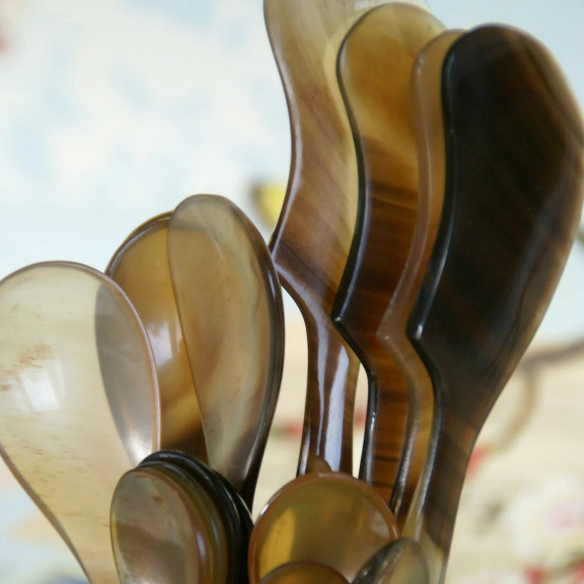 Four uniquely shaped and polished HORN SPREADERS by BE HOME, INC., handmade in Vietnam, are displayed against a warm mustard yellow background. Each spreader exhibits a distinct wavy design and a blend of dark and light natural hues.