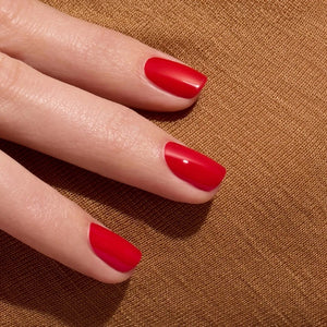 Twelve lipstick shades are presented with their names and color descriptions, spanning coral and brick reds to raspberries, cherries, and browns—each set against a backdrop of glossy swatches. These striking tones pair perfectly with the MANUCURIST - GREEN™ NAIL POLISH IN POPPY RED by MANUCURIST INC, a vibrant red nail polish crafted from bio-sourced ingredients for a coordinated and polished finish.