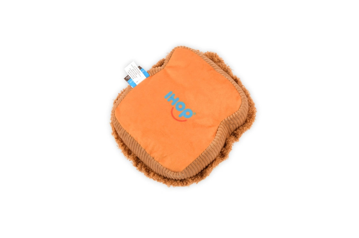 Close-up of the PLAY PET LIFESTYLE THICK ‘N FLUFFY FRENCH TOAST DOG TOY on a brown fabric with red and white patterns, pictured with plush strawberry and muffin toys.