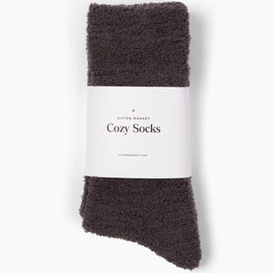 Beige fuzzy socks made from soft plush material are wrapped in a white "Cozy Cloud Socks" label displaying "Giften Market" and "GIFTENMARKET.COM." These women's socks are neatly folded and viewed from above on a plain background.